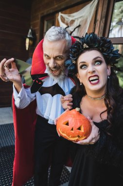 spooky couple in halloween vampires costumes grimacing with carved pumpkin and paper cut bat clipart