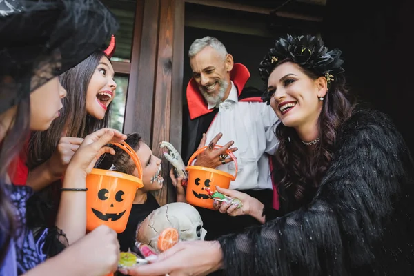 Happy Couple Halloween Costumes Giving Sweets Excited Kids Buckets — Stock Photo, Image