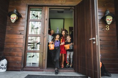 kids in spooky costumes running out neighbor house with halloween decoration clipart