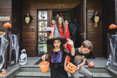 scared kids in halloween costumes screaming while running out house from spooky neighbors