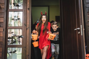 excited kids in halloween costumes shouting while running out neighbor house with buckets of sweets 