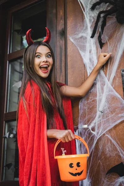 Excitado Chica Diablo Halloween Traje Celebración Cubo Mientras Golpea Puerta — Foto de Stock