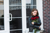 mladá žena v kožené bundě při pohledu na červené růže na městské ulici v Evropě 