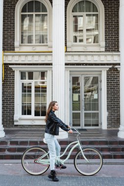Deri ceketli, bisiklet süren şık bir kadının yan görüntüsü. 