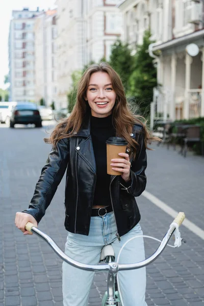 ヨーロッパの都会の通りで自転車に乗りながら紙コップを持っている幸せな女性 — ストック写真