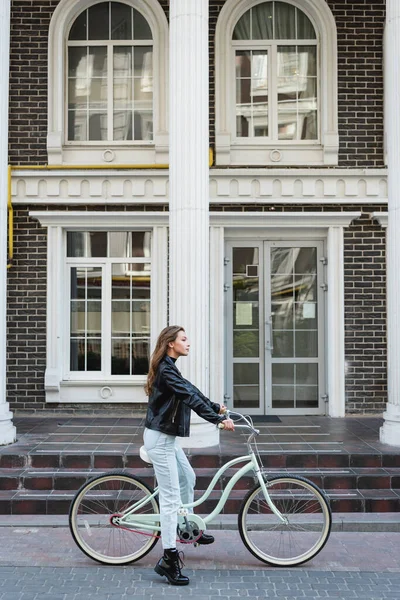 自転車に乗る革のジャケットのスタイリッシュな女性の側面図 — ストック写真