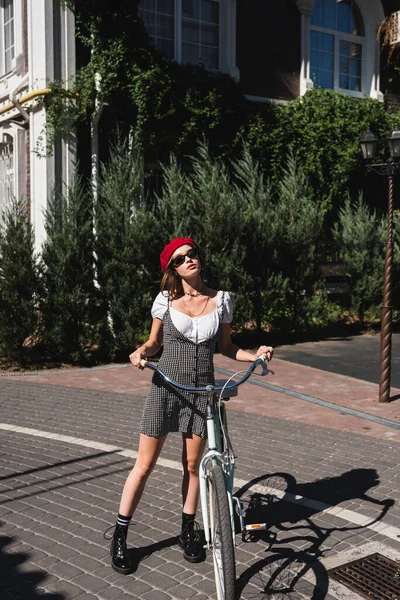 全尺寸的年轻女士太阳镜 红色贝雷帽 穿着自行车站在欧洲城市街道上 — 图库照片