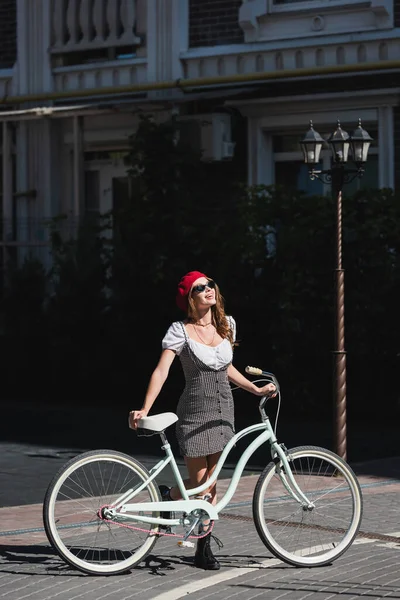 幸せな女性のサングラス 赤いベレー帽とヨーロッパの路上で自転車で立ってドレス — ストック写真