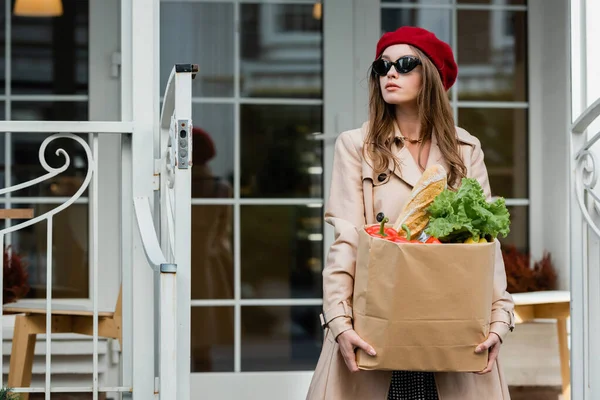 Ung Kvinna Beige Trenchcoat Röd Basker Och Solglasögon Hålla Papperspåse — Stockfoto