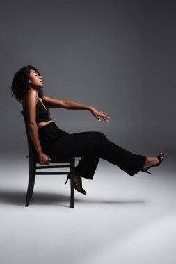 Koyu gri sandalyede oturan kıvırcık Afrikalı Amerikalı kadının yan görünüşü