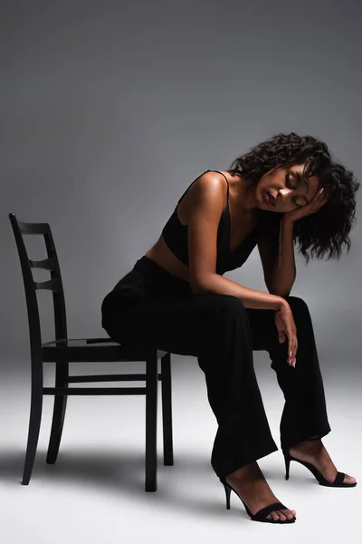 長さのブルネットアフリカ系アメリカ人女性でスタイリッシュな衣装で椅子に座っているグレー — ストック写真