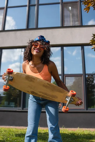 Mujer Afroamericana Positiva Sosteniendo Longboard Cerca Edificio Afuera —  Fotos de Stock