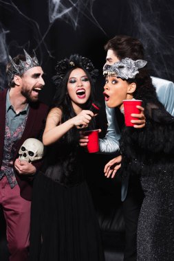 interracial women in halloween costumes singing karaoke near friends on black   clipart