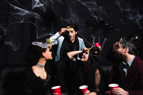 изумленный человек играет угадай, кто играет с межрасовыми друзьями в костюмах на Хэллоуин на черном