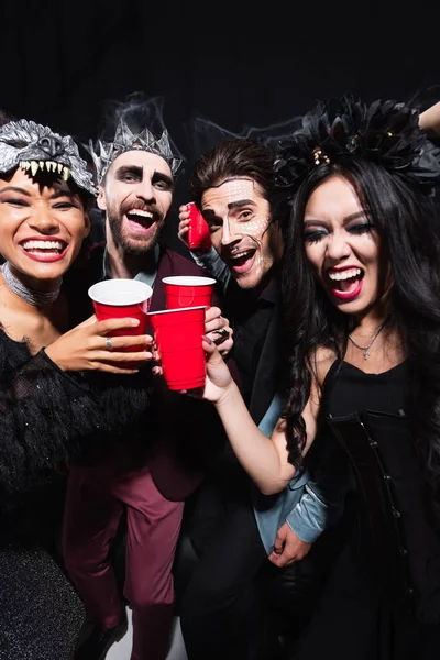Cheerful Multiethnic Friends Halloween Costumes Toasting Plastic Cups Black — Stock Photo, Image