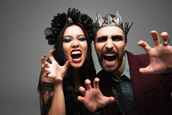 interracial couple in spooky vampires costumes growling and showing scary gesture at camera isolated on grey
