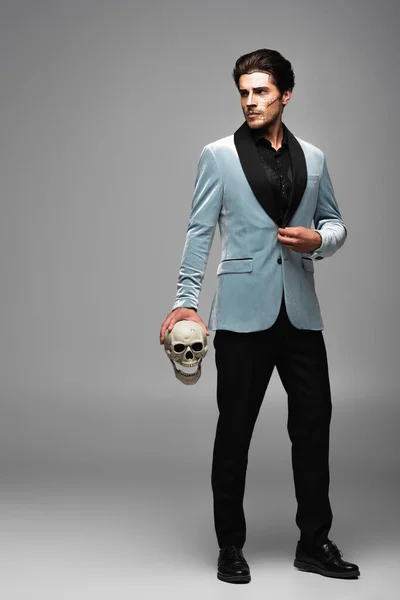灰色を見ながら恐ろしい頭蓋骨を持つエレガントなブレザーの男の完全な長さのビュー — ストック写真