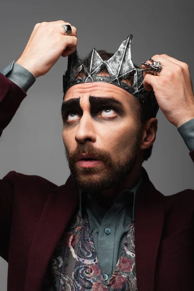Cadılar Bayramı makyajlı bir adam vampir kral tacını gri renkte izole ediyor.