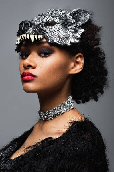 confident african american woman in wolf halloween mask and metal necklace looking at camera isolated on grey