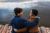 Seitenansicht eines positiven Paares, das sich auf einem Holzsteg am Meer umarmt 
