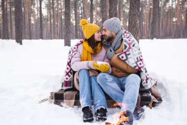 Bardak ve battaniyeli olumlu çiftin kış parkındaki bulanık şenlik ateşinin yanında birbirlerine bakışları. 