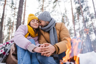 Genç çift, kış parkında gözleri kapalı, bulanık şenlik ateşinin yanında oturuyor. 