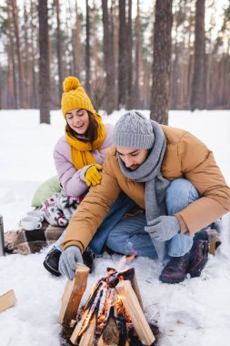 Kış parkında tahta kütüklerle erkek arkadaşına bakan gülümseyen bir kadın. 