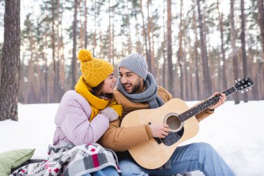 Mutlu çift kış parkında kar üzerinde akustik gitar çalıyor. 