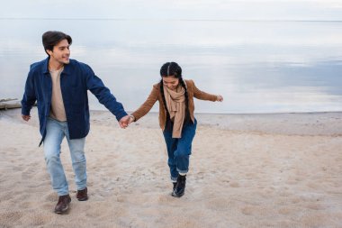 Kumsalda yürürken el ele tutuşan gülümseyen bir çift. 