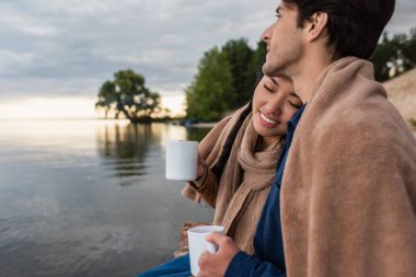 Gözleri kapalı gülümseyen Asyalı kadın elinde bardakla sevgilisinin ve gölünün yanında 