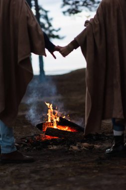 Bulanık bir çiftin akşam el ele tutuşması yakınındaki kamp ateşi manzarası. 
