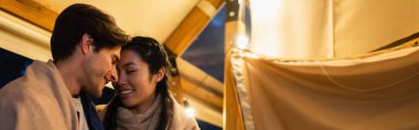 Gözü kapalı gülümseyen ırklar arası bir çift glamping evinin terasında, pankartta 