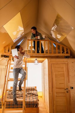 Tatil sırasında Glamping House 'da Asyalı kız arkadaşının yanındaki dizüstü bilgisayarı gösteren bir adam. 