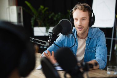 Kulaklıklı radyo sunucusu bulanık meslektaşına bakıyor ve podcast sırasında el kol hareketi yapıyor.