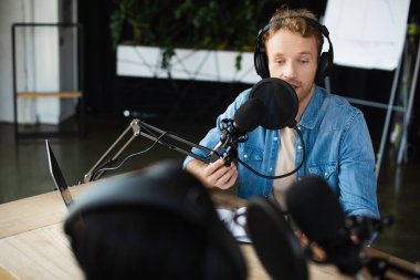 Kablosuz kulaklıkla radyo sunucusu mikrofonla konuşuyor ve podcast sırasında bulanık meslektaşına bakıyor.