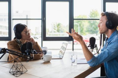 Irklar arası radyo sunucuları stüdyoda dizüstü bilgisayar ve içki yakınında podcast yapıyor. 