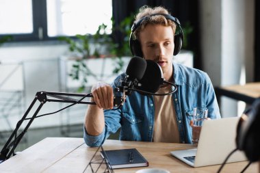 Podcast sırasında konuşurken kulaklıklı genç radyo sunucusu mikrofona dokunuyor.