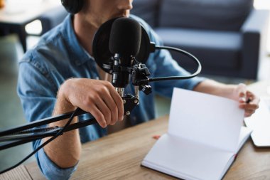 partial view of radio host in wireless headphones touching microphone stand in studio  clipart