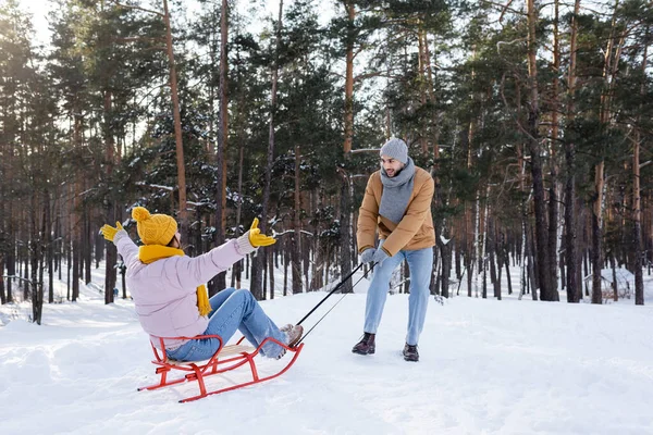 笑顔男引っ張っガールフレンド上の雪の上に公園 — ストック写真