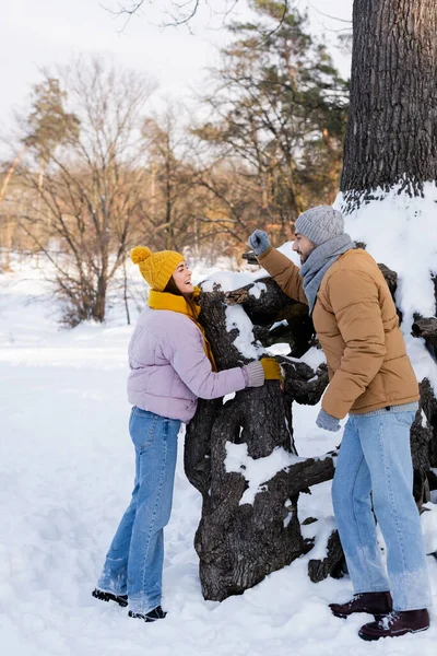 側ビューの笑顔の女性立って近くの木とともに雪とボーイフレンドで公園 — ストック写真
