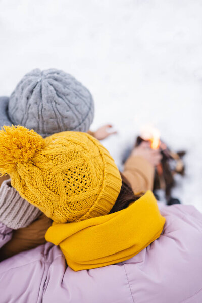 Overhead view of couple in knitted hats near blurred bonfire in winter park 