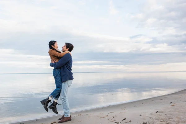 Side View Cheerful Man Lifting Asian Girlfriend Beach Sea Autumn — Stock Photo, Image