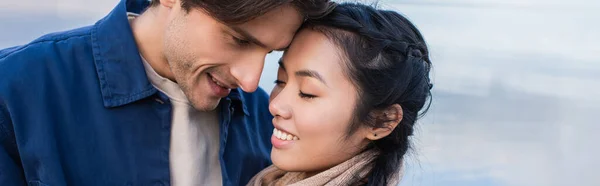 Sonriente Hombre Mirando Asiático Novia Cerca Borrosa Mar Fondo Bandera —  Fotos de Stock