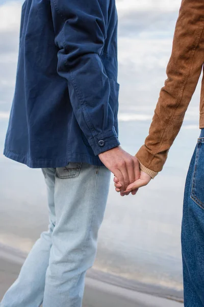 Cropped view of man holding hand of girlfriend on beach