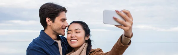 Asiática Mujer Tomando Selfie Con Sonriente Novio Cerca Mar Bandera — Foto de Stock