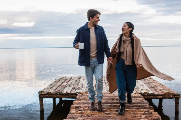 Pareja Multiétnica Positiva Con Taza Manta Caminando Muelle — Foto de Stock