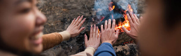 Blurred couple warming hands near campfire, banner 