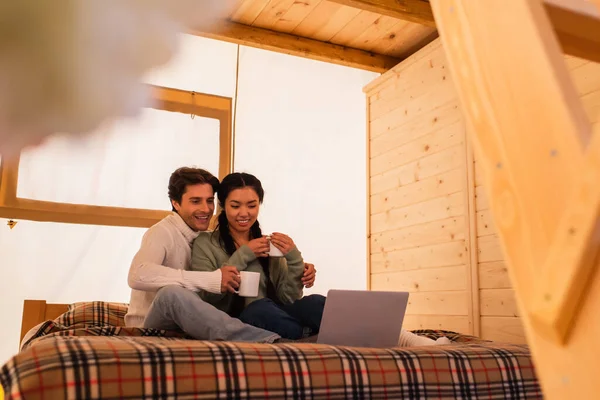 Smiling Multiethnic Couple Cups Looking Laptop Bed Glamping House — Stock Photo, Image