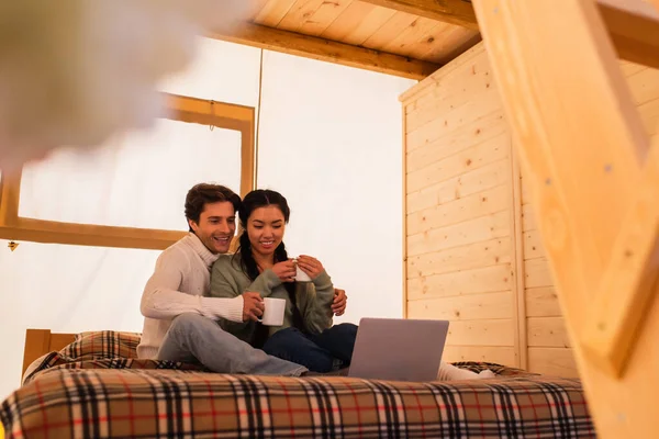 Smiling Multiethnic Couple Cups Looking Laptop Bed Glamping House — Stock Photo, Image