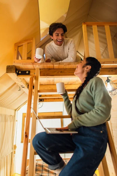 Vista Ángulo Bajo Sonriente Pareja Interracial Con Tazas Portátil Mirándose — Foto de Stock